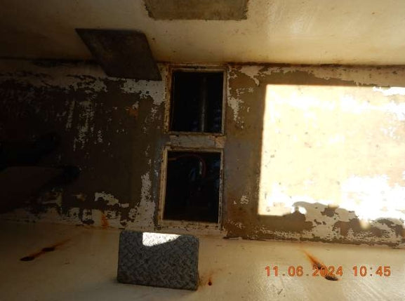 A worn interior wall with peeling paint, two dark rectangular openings, a bright sunlit patch on the right, and a timestamp in orange at the bottom right.