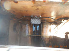 Close-up view of the underside of a rusty metal structure or machinery component, showing pipes, bolts, and a textured rectangular plate. A timestamp in orange appears in the bottom right corner.
