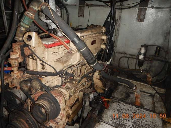 A used, dirty marine diesel engine with hoses, belts, and wiring, photographed inside a cramped engine room. An orange timestamp is visible in the bottom right corner.