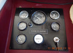 A vintage marine instrument dashboard with multiple round analog gauges mounted on a black panel, featuring a central tachometer and a label reading 'CUMMINS MARINE'.