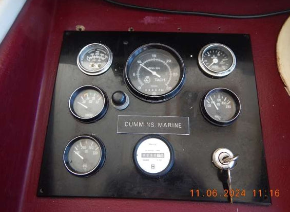 A vintage marine instrument dashboard with multiple round analog gauges mounted on a black panel, featuring a central tachometer and a label reading 'CUMMINS MARINE'.