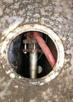 Metal pipe with a pink hose inside a circular metal cover on a concrete surface.