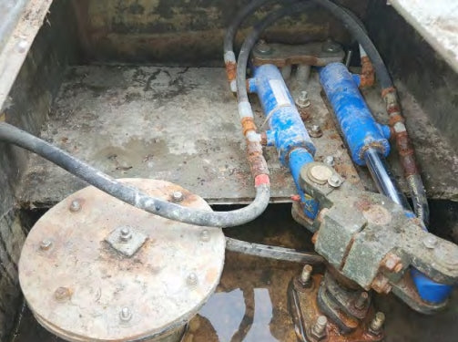 Rust-covered hydraulic system with blue cylinders and metal components.