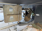 Close-up of a boat's stern mechanical area showing a large metal rudder, a bronze propeller, and part of the dark hull in a snowy outdoor setting.