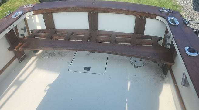 A curved wooden bench with white upholstered back cushions installed inside a boat cabin, viewed from above on a white deck.
