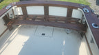 A curved wooden bench with white upholstered back cushions installed inside a boat cabin, viewed from above on a white deck.