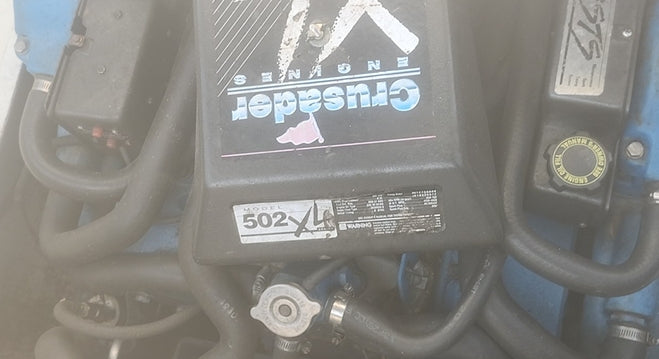 A close-up of a black engine cover labeled 'Cruiser' and '502 XL4' with visible hoses and surrounding mechanical components.