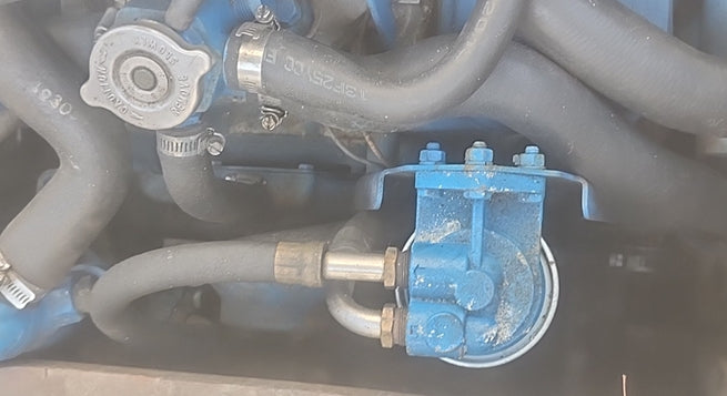 A close-up of a blue mechanical pump or valve component attached to gray and blue hoses on an engine.