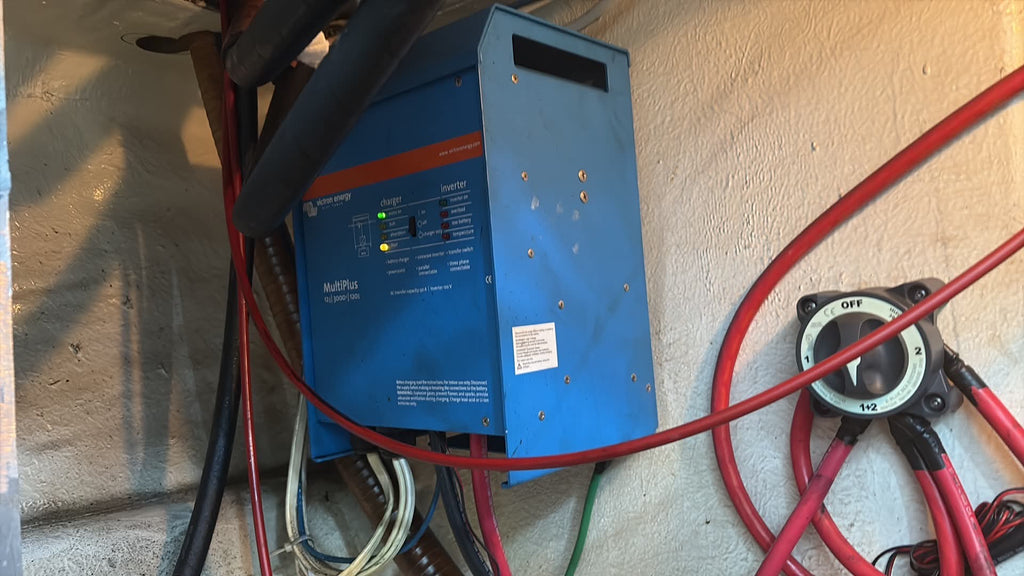 A blue marine battery charger or marine electrical device mounted on a concrete wall, surrounded by red and black cables connected to a marine battery or alternator.