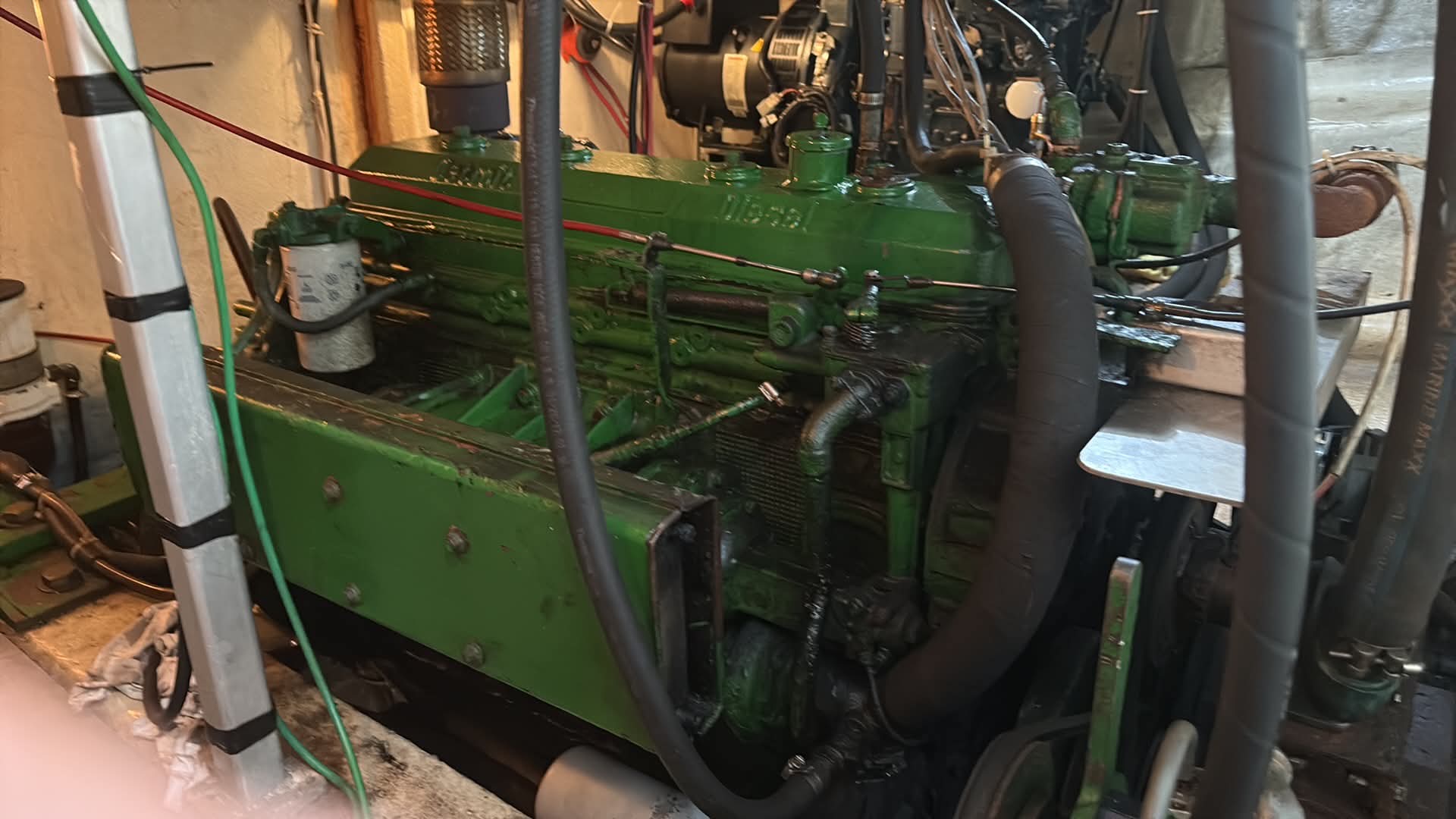 A large green industrial engine or generator with hoses, pipes, and metal components, photographed in a workshop or garage setting.