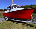 A red and white wooden fishing boat on a metal trailer, parked outdoors on a grassy gravel area under a blue sky.