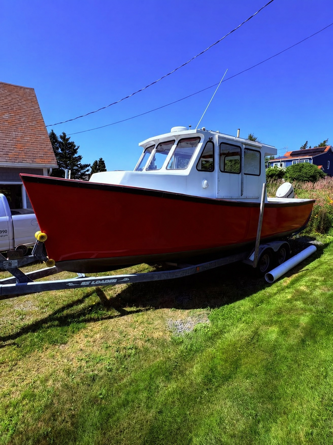 A red and white fishing boat on a metal trailer parked on a grassy lawn outdoors under a clear blue sky.