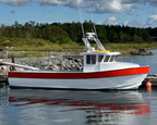 A white fishing boat with a red stripe along the hull is docked at a harbor under a blue sky with large white clouds. Trees and rocks line the shore in the background, with another boat and dock structures visible.