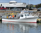 A white fishing boat with a red stripe along the hull, docked in calm water with a harbor and industrial buildings in the background.