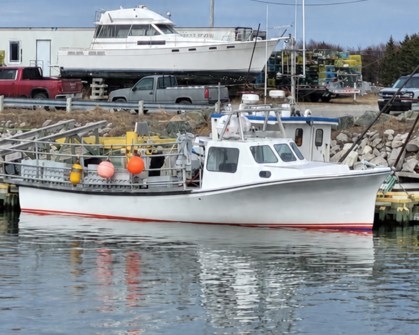 A white fishing boat with a red stripe along the hull, docked in calm water with a harbor and industrial buildings in the background.