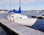 Marina scene with sailboats docked at a wooden pier on a clear day.