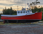 Red and white boat on a gravel area with trees and water in the background