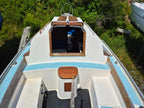 Top view of a boat with white interior and wooden elements, surrounded by greenery.