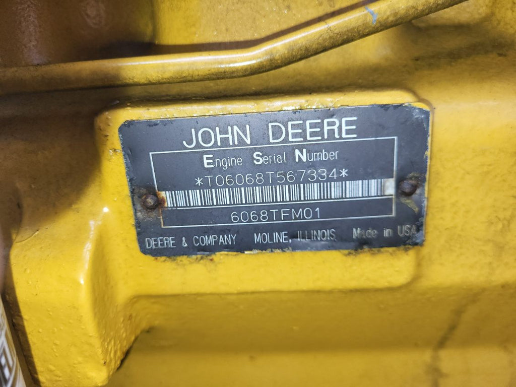 A close-up of a John Deere engine serial number plate mounted on a yellow painted metal housing.