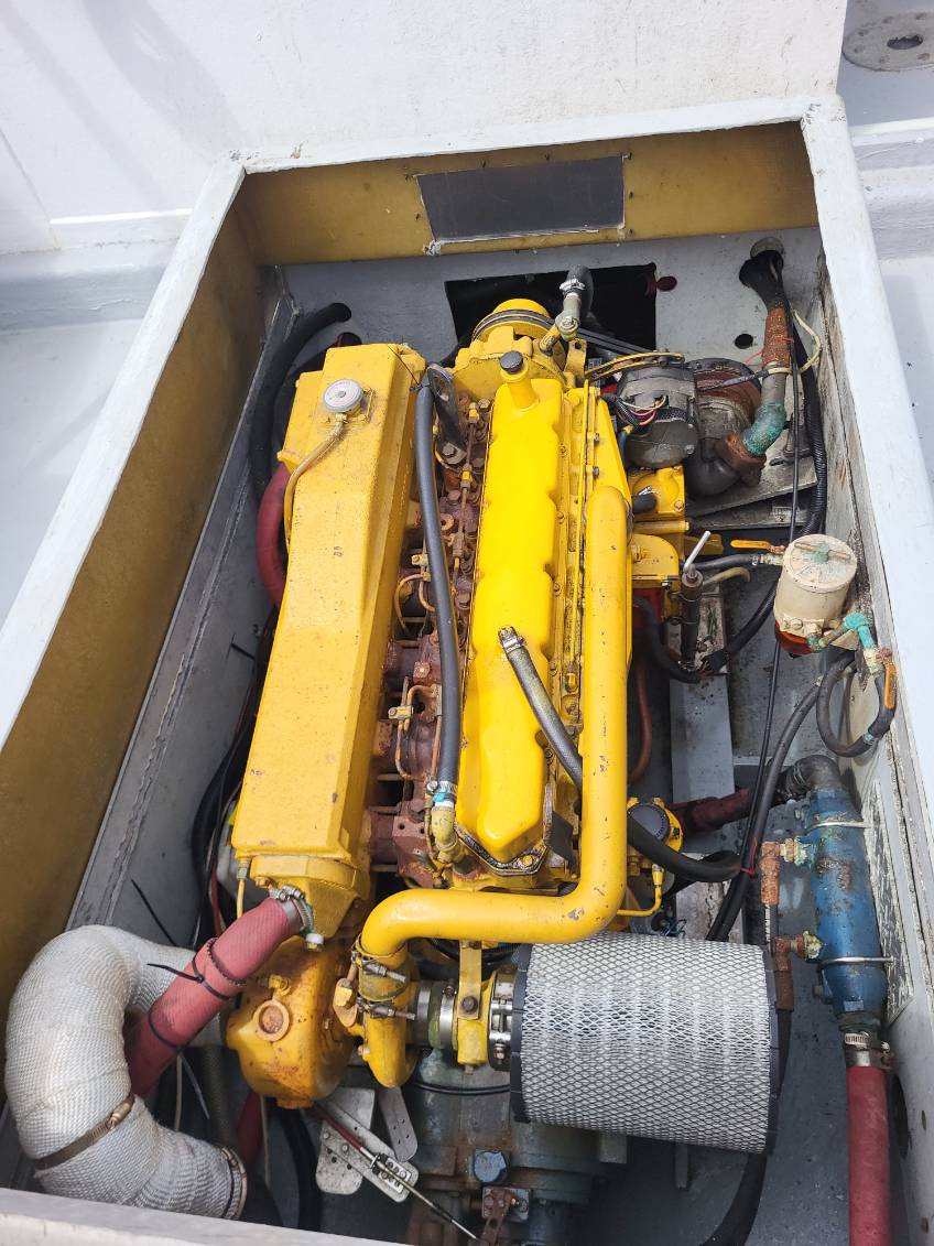 A large yellow marine engine housed inside a white compartment, with visible hoses, wires, metal parts, and a silver air filter.