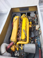 A large yellow marine engine housed inside a white compartment, with visible hoses, wires, metal parts, and a silver air filter.