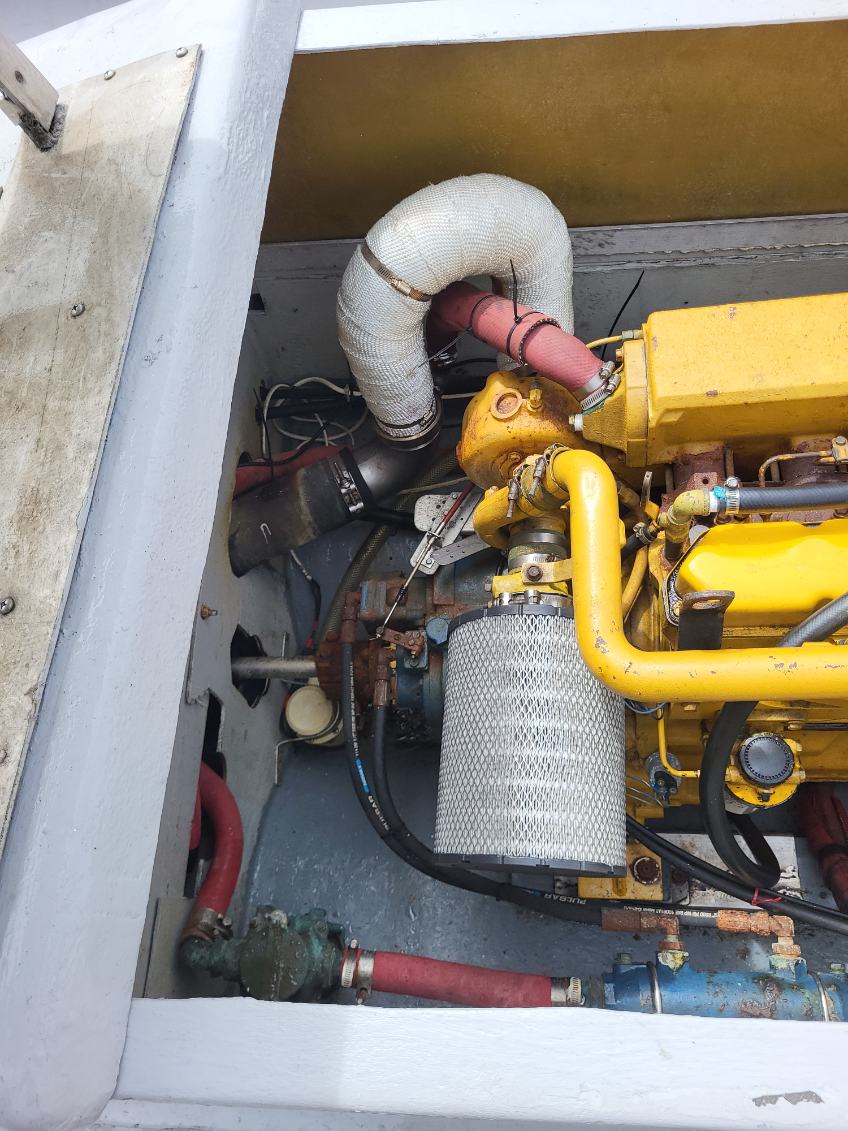 Close-up of a yellow industrial engine compartment with a large silver air filter, corrugated white intake hose, black hoses, and red pipes inside a gray metal housing.