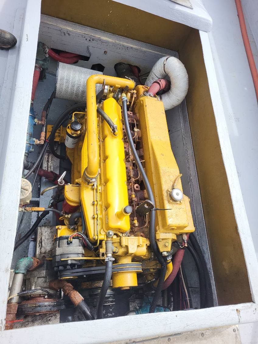 A large yellow industrial marine engine housed inside a white metal casing, with various hoses, wires, and mechanical components visible.