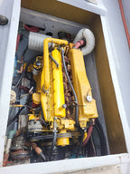 A large yellow industrial marine engine housed inside a white metal casing, with various hoses, wires, and mechanical components visible.