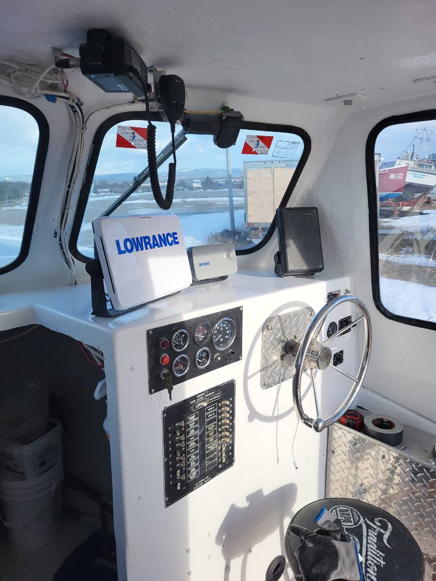 A white boat cabin interior with a Lowrance radar unit, steering wheel, instrument panel, and windows looking out onto a snowy outdoor area.