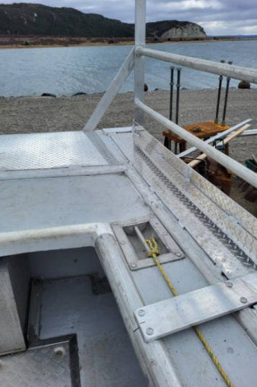 A close-up view of a white metal boat deck or railing structure near water, with a shoreline and hills in the background. The photo appears to be taken from within the boat and is shown inside a mobile app interface with an 'Edit with AI' button visible.