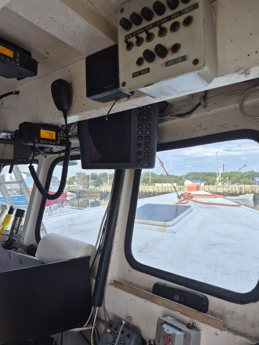 The interior of a boat's navigation bridge with various electronic instruments, including a radar screen, a VHF radio, a speaker, and control panels mounted on the beige walls.