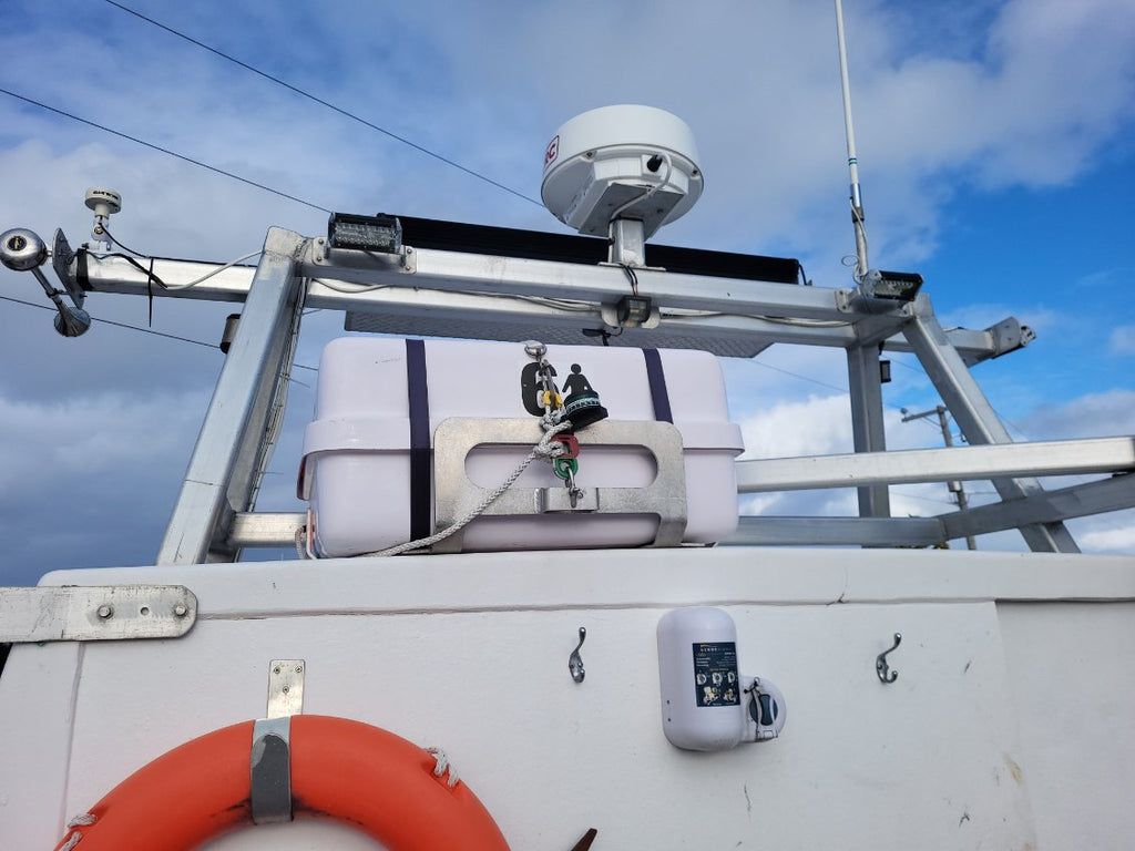 A close-up view of a white boat or vessel deck with a metal mounting frame, a white radar or communication antenna dome, a small bell, and an orange life preserver against a blue sky with clouds.
