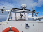 A close-up view of a white boat or vessel deck with a metal mounting frame, a white radar or communication antenna dome, a small bell, and an orange life preserver against a blue sky with clouds.