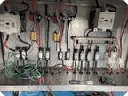 An electrical panel or control cabinet interior with multiple circuit breakers, fuses, wires, terminal blocks, and metal components arranged on a metal chassis.