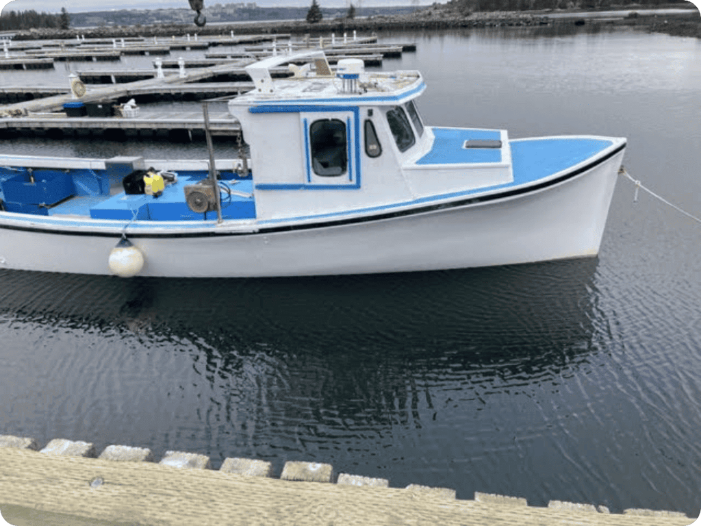 A small white and blue fishing boat moored at a dock in calm water, with wooden piers and shoreline visible in the background.