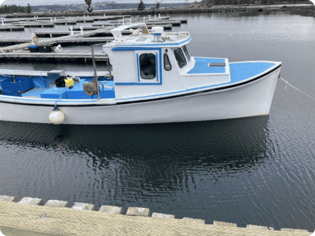 A small white and blue fishing boat moored at a dock in calm water, with wooden piers and shoreline visible in the background.