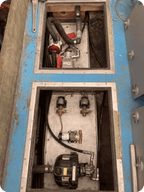 Open blue and gray industrial machinery compartments showing internal pumps, hoses, valves, and metal piping.