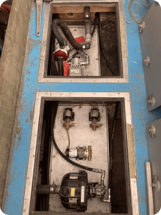 Open blue and gray industrial machinery compartments showing internal pumps, hoses, valves, and metal piping.